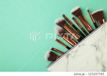 Cosmetic bag with different brushes of professional makeup artist on mint background 125207765