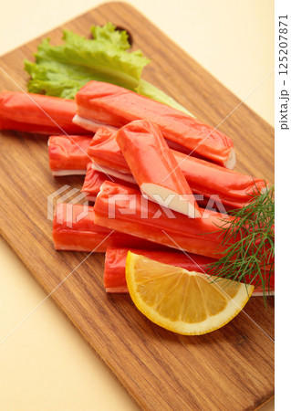 Fresh crab sticks with lemon on cutting board on beige background. Fresh crab sticks with lemon on cutting board on beige background. 125207871