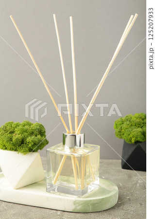 Aromatic reed air freshener and green plant on grey background 125207933