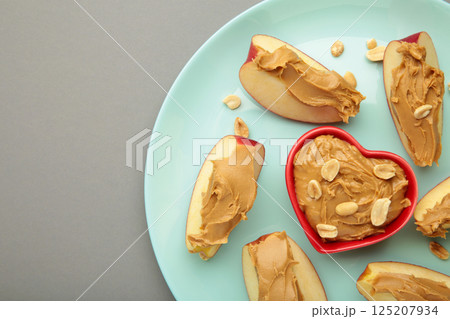 Slices of fresh apple with peanut butter in bowl on mint plate on grey background. Slices of fresh apple with peanut butter in bowl on mint plate on grey background. 125207934