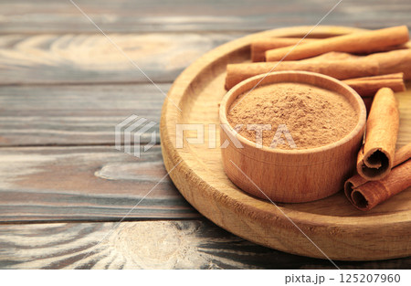 Cinnamon sticks and powder in wooden bowl on brown background. Space for text 125207960