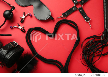 BDSM set on red background. BDSM accessories and rope in the shape of a heart. Mask, handcuffs, ball gag and a whip. BDSM set on red background. BDSM accessories and rope in the shape of a heart. Mask, handcuffs, ball gag and a whip. 125208107