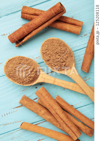 Cinnamon sticks and powder in wooden spoon on blue wooden background. Cinnamon sticks and powder in wooden spoon on blue wooden background. 125208118