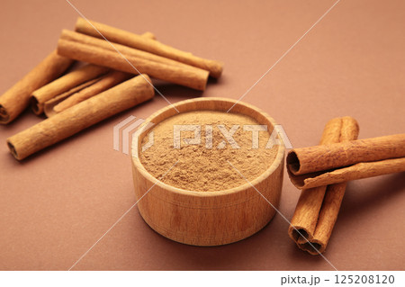 Cinnamon sticks and powder in wooden bowl on brown background. Cinnamon sticks and powder in wooden bowl on brown background. 125208120