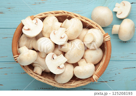 Fresh champignon mushrooms in basket on blue background. Fresh champignon mushrooms in basket on blue background. 125208193