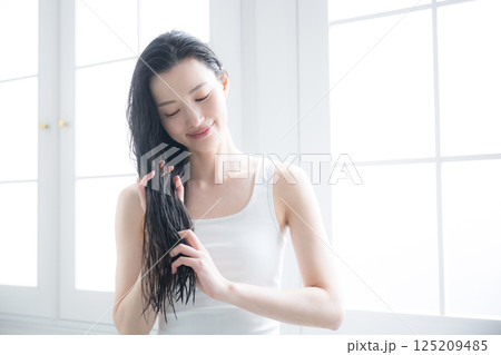 若い女性の濡れた髪のヘアオイルを塗るトリートメント　毛先の枝毛などをケアするイメージ 125209485