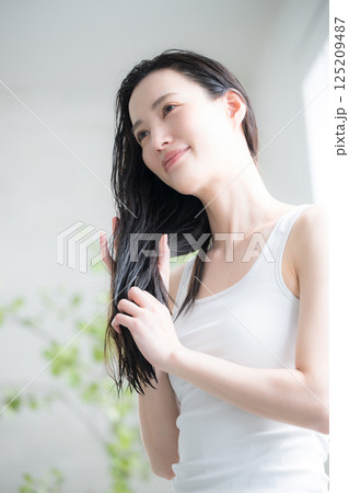 若い女性の濡れた髪のヘアオイルを塗るトリートメント　毛先の枝毛などをケアするイメージ 125209487
