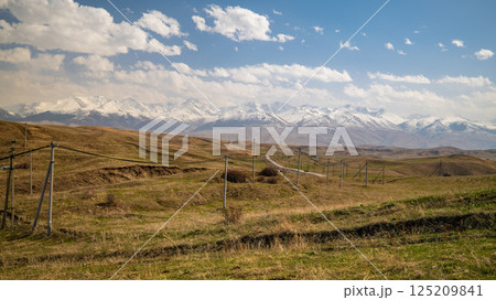 Panoramic mountain landscape with winding road through vast steppe and snow capped peaks 125209841