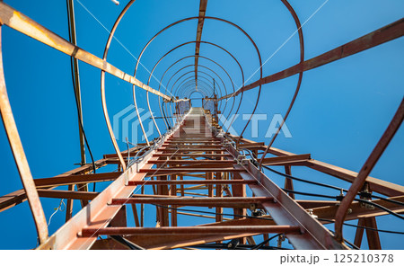 Looking up inside telecommunications tower safety ladder against blue sky perspective Looking up inside telecommunications tower safety ladder against blue sky perspective 125210378