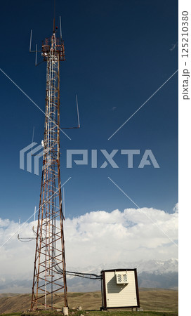 Telecommunications tower on hilltop with equipment cabins against blue sky and clouds Telecommunications tower on hilltop with equipment cabins against blue sky and clouds 125210380