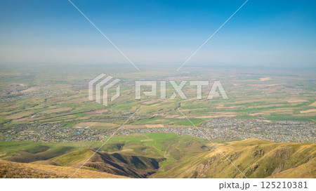 Aerial panoramic view of agricultural landscape with foothills and distant settlements under clear blue sky 125210381