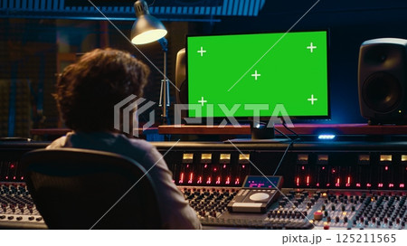 Sound designer watches online tutorials via greenscreen monitor to mix and master tracks and create music for his album. Audio engineer producing songs by twisting knobs and pushing faders. Camera A. 125211565