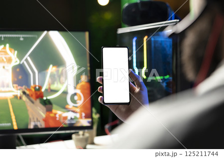 Man looking at mockup phone while playing SF FPS videogame, having fun in dark apartment room. Gamer holding isolated screen smartphone, competing in PvP internet multiplayer game, close up Man looking at mockup phone while playing SF FPS videogame, having fun in dark apartment room. Gamer holding isolated screen smartphone, competing in PvP internet multiplayer game, close up 125211744