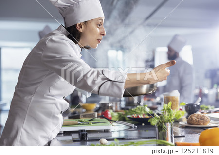 Skilled chef working over a stovetop cooking vegetables in oil with kitchen tools and utensils. Woman expert at the kitchen counter preparing fresh produce, emphasizing the artistry of food prep. Skilled chef working over a stovetop cooking vegetables in oil with kitchen tools and utensils. Woman expert at the kitchen counter preparing fresh produce, emphasizing the artistry of food prep. 125211819