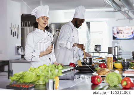 Head chef stands at a kitchen counter and chopping vegetables, using stainless steel tools to prepare and cook a delicious gourmet dish. Culinary expert cooking with raw materials in the kitchen. 125211868