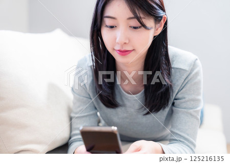 ソファでリラックスをしてスマホを使う若い女性 125216135