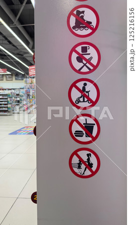 Vertical photo with sticker icons at entrance to store. Signs in red circle with prohibiting actions in store. Strict restrictions in retail space 125216156