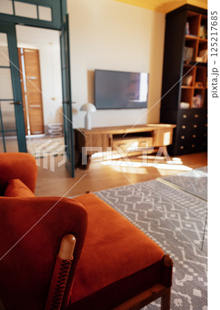 Close-up details of an elegant armchair made of orange fabric and wooden elements. Modern living room with wooden furniture. Bright sunlight. 125217685
