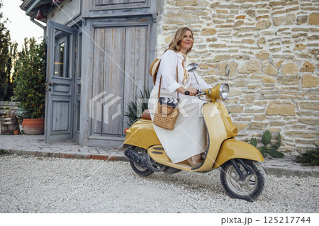 Beautiful female driver in white shirt and beige dress driving yellow motoroiler. Beautiful female driver in white shirt and beige dress driving yellow motoroiler. 125217744
