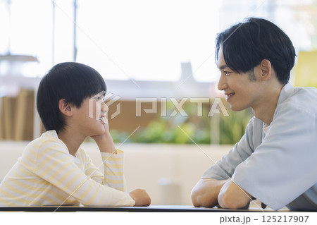 父親と息子の会話イメージ　テーブルで向き合う小学生の男の子と話す30代の男性 125217907