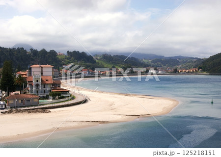 A view of the Ribadesella`s sandy beach, estuary of the river Silla, green hills, mountains, buoy and a promenade along houses with red tiled roofs A view of the Ribadesella`s sandy beach, estuary of the river Silla, green hills, mountains, buoy and a promenade along houses with red tiled roofs 125218151