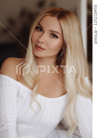 Blonde woman in white dress lying on bed with canopy 125218450