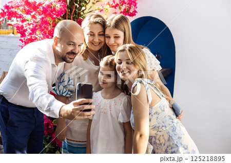 A happy family is photographed at a festive event. A joyful man takes a selfie with his three daughters and his wife. 125218895