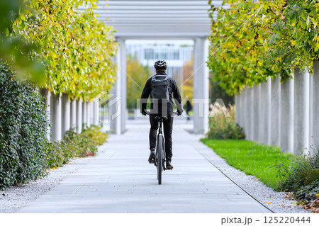 Employee commuting by bike along a green urban pathway, promoting clean transportation Employee commuting by bike along a green urban pathway, promoting clean transportation 125220444