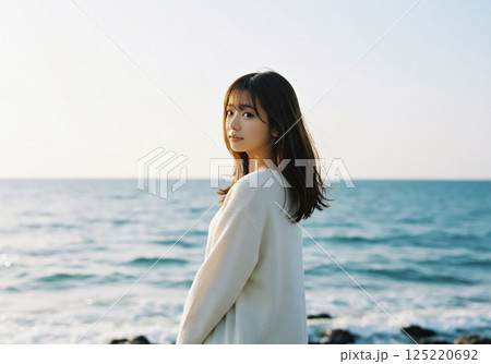 海を背景に振り返るニットを着た女性 125220692