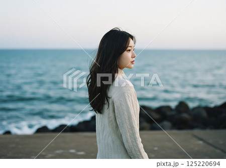 風が吹く海沿いに佇む女性 125220694