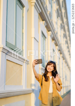 Traveler asian woman in her 30s making a livestream and selfie with a smartphone enjoying travel in Bangkok, Thailand. Journey trip lifestyle, world travel explorer or Asia summer tourism concept. 125221683