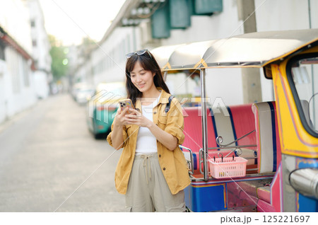 Young Asian woman backpack traveler standing a side of Tuk Tuk taxi on summer vacations at Bangkok, Thailand. Journey trip lifestyle, Asia summer tourism concept. 125221697