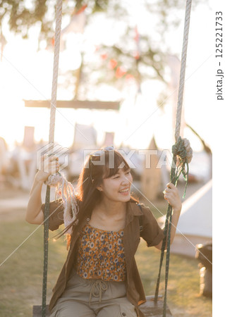 asian woman sitting in swing at camping site. asian woman sitting in swing at camping site. 125221733
