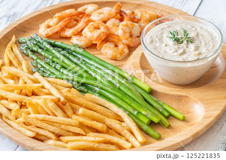 Rustic wooden tray serves full meal of shrimp, asparagus, fries, and sauce 125221835
