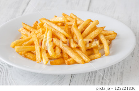 Golden fries piled high on white plate resting on rustic white table Golden fries piled high on white plate resting on rustic white table 125221836