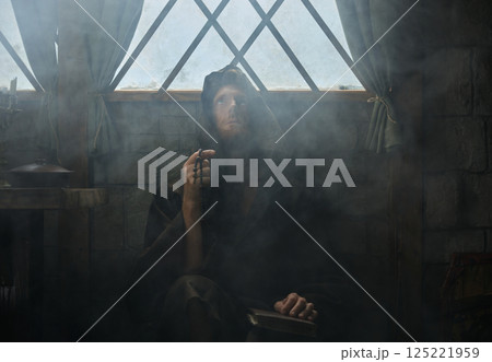 Mystery shot of clergyman holding rosary beads and bible praying surrounded mist 125221959