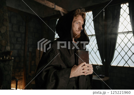 Medieval priest holding closed bible book and rosary beads in hands closeup 125221960
