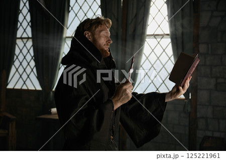 Medieval priest holding cross and holy bible performing exorcism rite 125221961