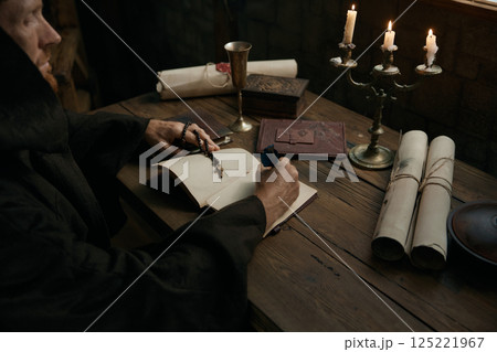 Crop shot of medieval monk chronicler writing ancient manuscript under candlelight Crop shot of medieval monk chronicler writing ancient manuscript under candlelight 125221967