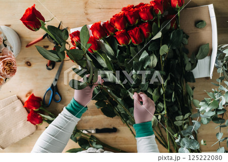 Florist preparing red roses for bouquet arrangement on wooden worktable. Showcases artisan craftsmanship, floral entrepreneurship, and handmade design trends 125222080