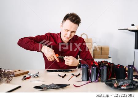 Jewelry artisan assembling a handmade earring at a studio table filled with tools and gift packaging. DIY jewelry, microbusiness, creative entrepreneurship, artisanal brand 125222093