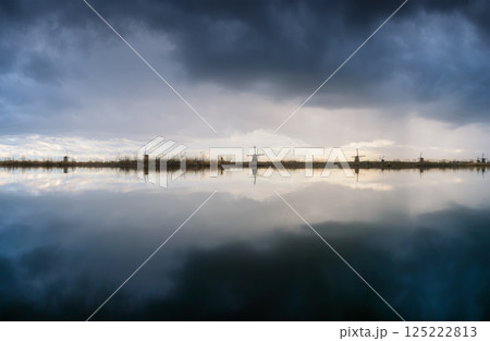 Windmills in the Netherlands during sunset. Storm clouds and sun glow. Dutch canals. 125222813