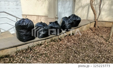 A row of black garbage bags is lined up neatly outside, showcasing urban waste disposal efforts A row of black garbage bags is lined up neatly outside, showcasing urban waste disposal efforts 125223773