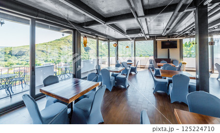 Inviting Modern Restaurant Interior with Scenic Views of Lush Green Hills and Abundant Natural Light, Perfect for Dining or Relaxation in a Stylish Atmosphere 125224710