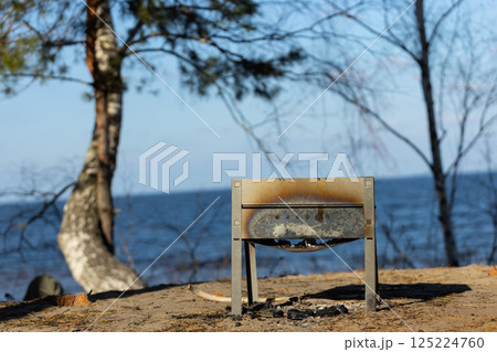 A Charred Grill By The Tranquil Water: An Abandoned Scene of Nature and Memories Evoked by a Burnt Grill Beneath Towering Trees at The Edge of a Beautiful Lake A Charred Grill By The Tranquil Water: An Abandoned Scene of Nature and Memories Evoked by a Burnt Grill Beneath Towering Trees at The Edge of a Beautiful Lake 125224760