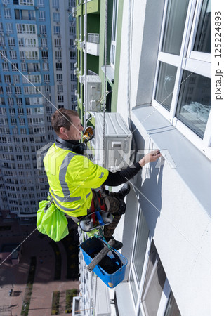 High-Rise Window Cleaner at Work: A Brave Worker Operating on the Edge of Tall Building, Demonstrating Professionalism in Extreme Conditions on a Bright Day High-Rise Window Cleaner at Work: A Brave Worker Operating on the Edge of Tall Building, Demonstrating Professionalism in Extreme Conditions on a Bright Day 125224893