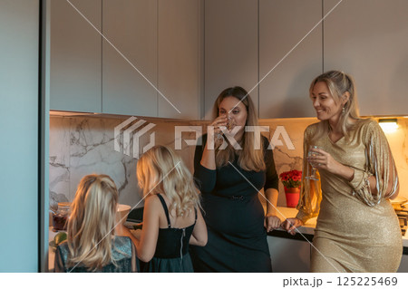 Women, Kitchen, Gathering: Friends enjoy drinks, conversation, and snacks in modern home kitchen during evening get-together. Women, Kitchen, Gathering: Friends enjoy drinks, conversation, and snacks in modern home kitchen during evening get-together. 125225469