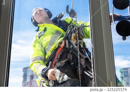 A Dedicated Window Cleaner Working at Heights, Ensuring Safety and Clarity in a Modern Urban Environment with a Bright Blue Sky Above 125225574