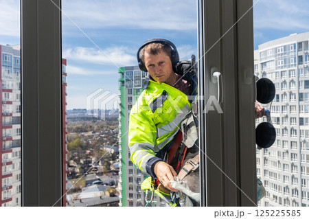 Window Cleaner at High Rise Building: A Dedicated Worker in Safety Gear Performing His Job with Precision from an Elevated Height Overlooking the Cityscape Below 125225585