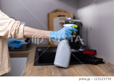 A Person in Gloves Preparing to Clean a Kitchen Surface with a Spray Bottle, Showcasing a Household Cleaning Routine with Attention to Hygiene and Cleanliness in a Modern Home Environment 125225739